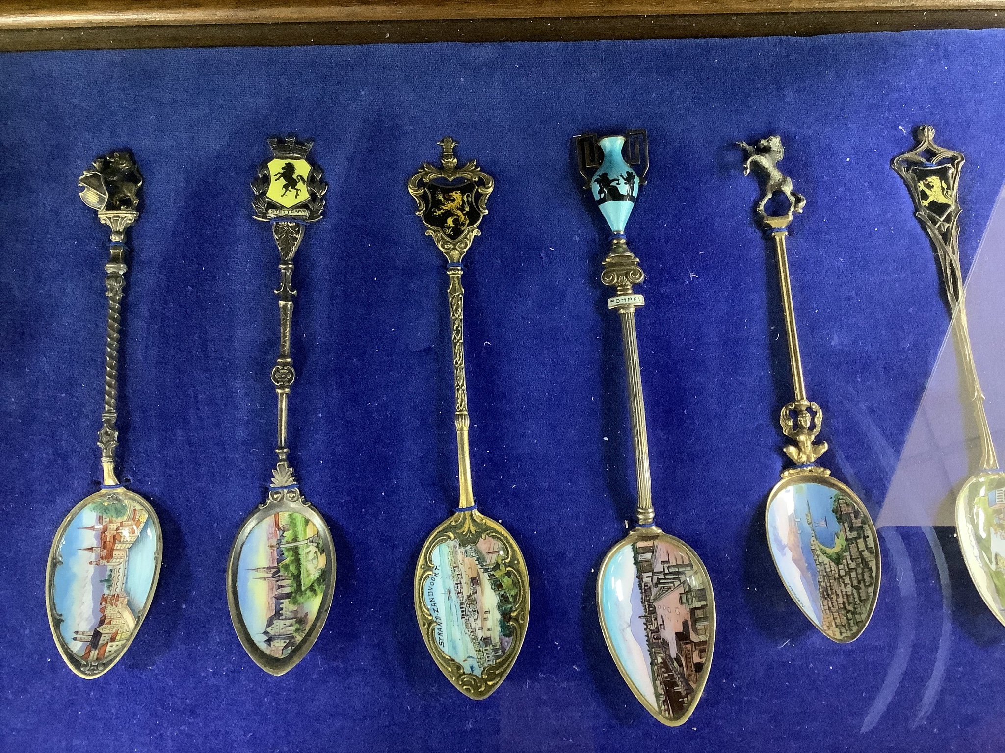 A collection of sixty four 800 standard silver (many gilt) and enamel souvenir spoons, early 20th century, in eight display cases, Including views of London, Germany, Italy, Austria, Spain etc.